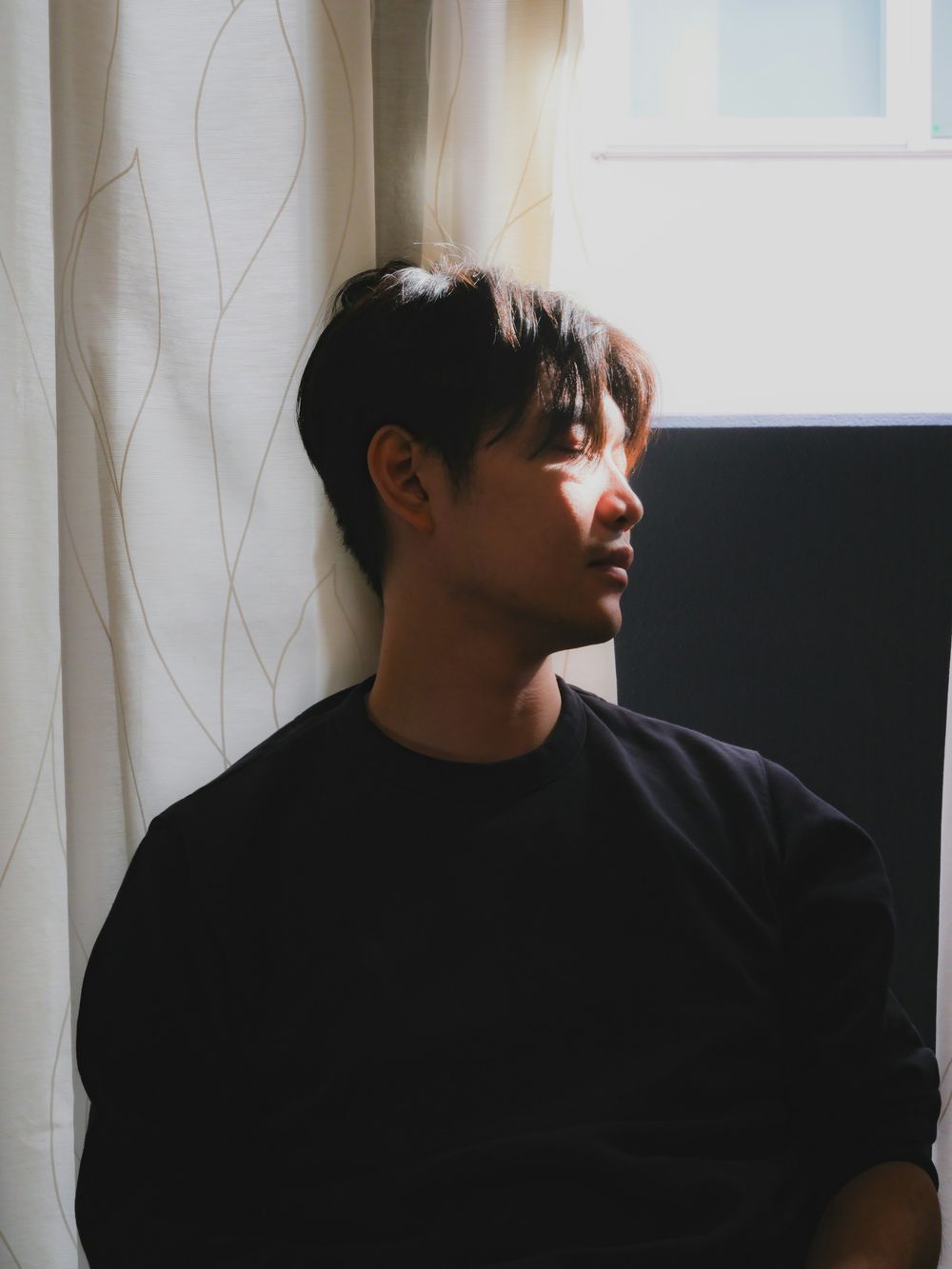 A young man lit by soft daylight from a window beside him