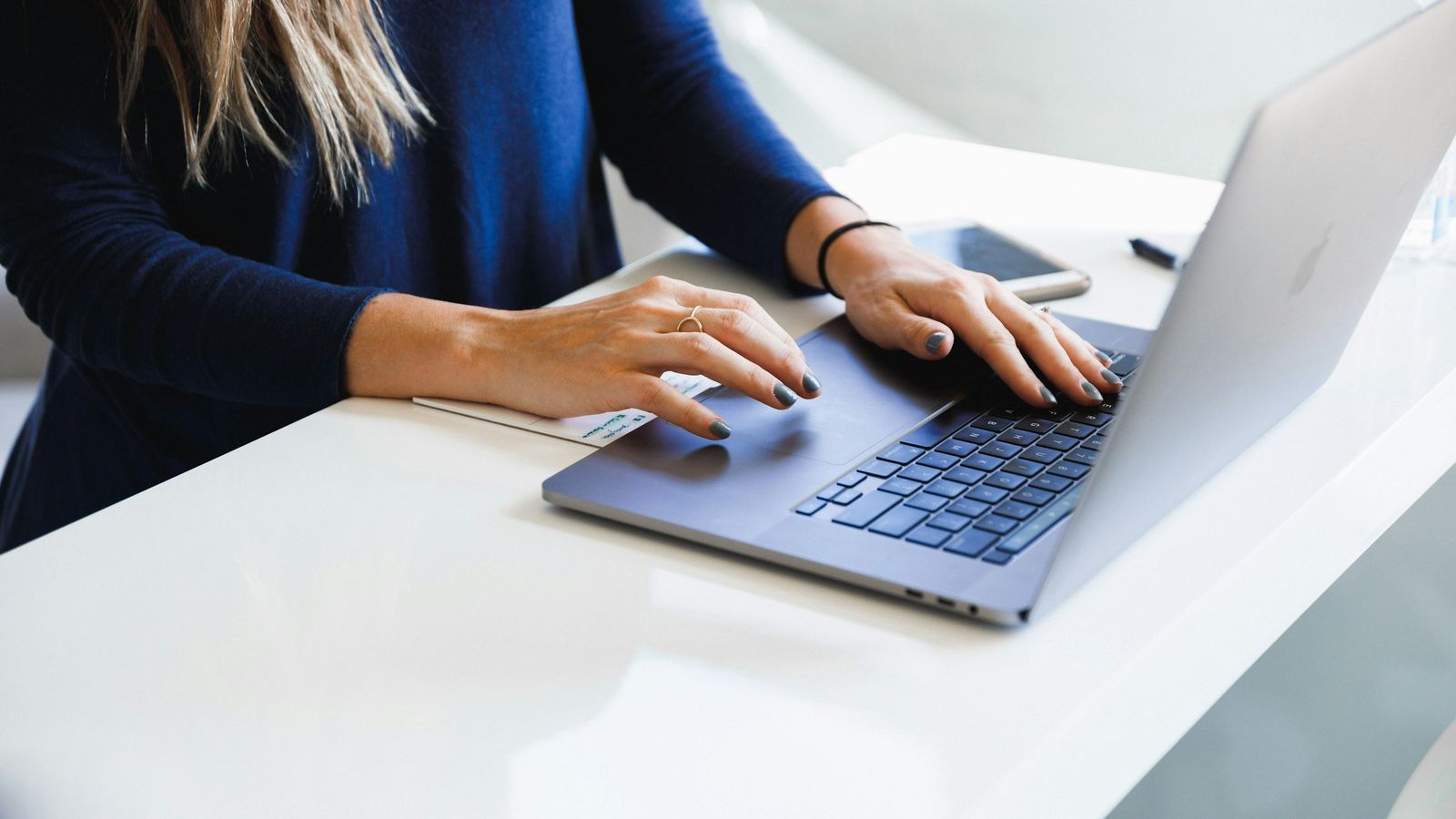 A woman typing an email on a laptop at a white desk